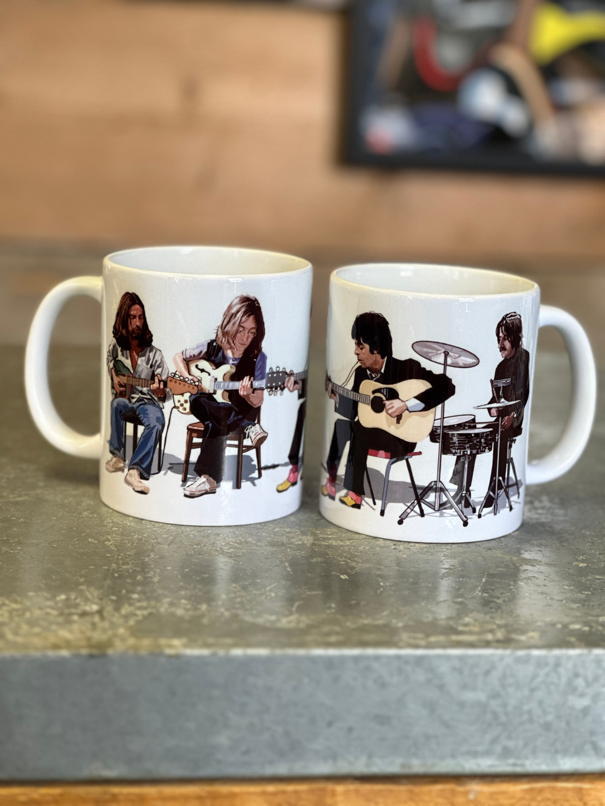 Two white ceramic mugs with printed band photos, displayed side-by-side on a gray countertop with a wooden wall in the background.